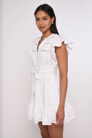 Love the Label Madelyn Mini Dress in bright white featuring flutter sleeves, lace inset details, a tie waist, and tiered ruffle hem