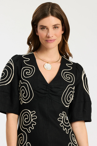 Model wearing Tyler Boe Posey Linen Midi Dress in black linen with white contrast embroidery, lantern sleeves, and midi silhouette
