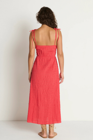 Model wearing the Nation LTD Madeline Tie Midi Dress in Flora, a coral pink textured midi dress featuring adjustable tie straps, shirred detailing, smocked voile fabric, a fitted bodice, and a flowing skirt.