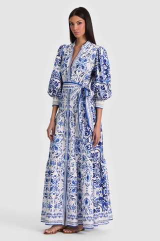 Model wearing the Alice + Olivia Cora Maxi Shirt Dress in Solstice featuring a blue-and-white porcelain-inspired print, blouson sleeves, adjustable tie waist, tiered maxi skirt, and lightweight cotton voile fabrication paired with flat sandals
