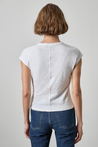 A woman viewed from the back wearing a white short-sleeve top with a vertical seam down the center and blue jeans, against a light gray studio background.