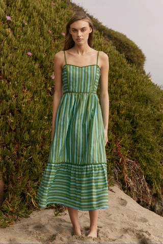 Woman wearing a green and blue striped dress standing against a natural background.
