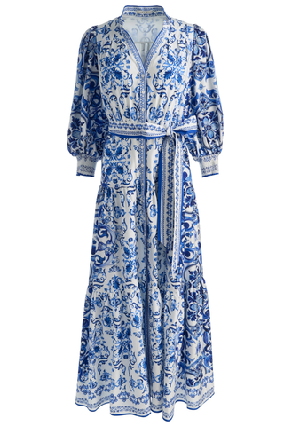 Model wearing the Alice + Olivia Cora Maxi Shirt Dress in Solstice featuring a blue-and-white porcelain-inspired print, blouson sleeves, adjustable tie waist, tiered maxi skirt, and lightweight cotton voile fabrication paired with flat sandals