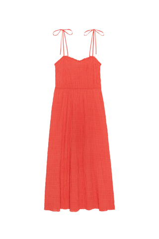 Model wearing the Nation LTD Madeline Tie Midi Dress in Flora, a coral pink textured midi dress featuring adjustable tie straps, shirred detailing, smocked voile fabric, a fitted bodice, and a flowing skirt.