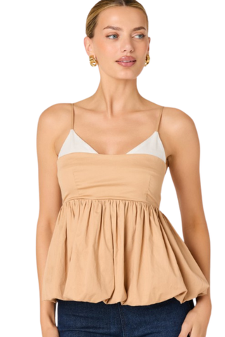 Woman wearing a tan and white two-tone top with spaghetti straps and bubble hem from ASTR paired with dark denim on a white background.