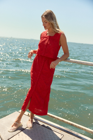 Model wearing the Olivia by Livro Fawn Skirt in Netta featuring vibrant coral eyelet embroidery, a midi-length straight silhouette, covered button front detailing, and matching coordinating top styled with lace-up sandals by the water