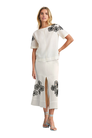 Woman wearing a white outfit with black floral embroidery on a white background