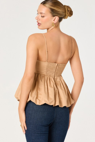 Woman wearing a tan and white two-tone top with spaghetti straps and bubble hem from ASTR paired with dark denim on a white background.