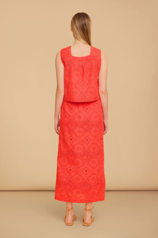 Model wearing the Olivia by Livro Fawn Skirt in Netta featuring vibrant coral eyelet embroidery, a midi-length straight silhouette, covered button front detailing, and matching coordinating top styled with lace-up sandals by the water