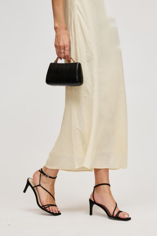 Rue Aveline Nichelle Clutch in Black featuring a textured structured exterior, sculptural gold-tone top handle, and removable chain strap.