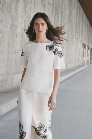 Woman wearing a white outfit with black floral embroidery in an urban setting.