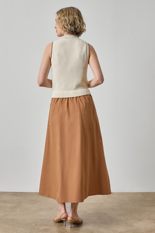 Woman wearing a cream sleeveless top and brown skirt against a plain background