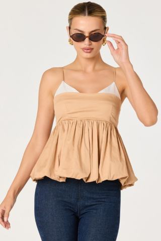 Woman wearing a tan and white two-tone top with spaghetti straps and bubble hem from ASTR paired with dark denim on a white background.