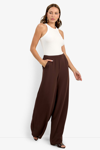 Woman wearing a white sleeveless top and brown wide-leg pants on a white background