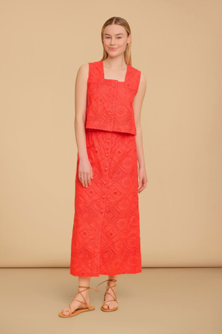 Model wearing the Olivia by Livro Nellie Top in Netta featuring vibrant coral eyelet embroidery, a sleeveless cropped silhouette, square neckline, covered button front detailing, and coordinating matching skirt styled with lace-up flat sandals