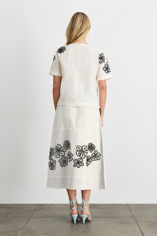 Woman wearing a white dress with black floral embroidery on a plain background