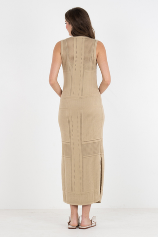 Model wearing the Emily McCarthy Bali Dress in Sand featuring a sleeveless open-knit design, midi length silhouette, textured detailing, and side slit accents
