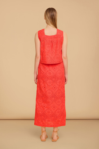 Model wearing the Olivia by Livro Nellie Top in Netta featuring vibrant coral eyelet embroidery, a sleeveless cropped silhouette, square neckline, covered button front detailing, and coordinating matching skirt styled with lace-up flat sandals