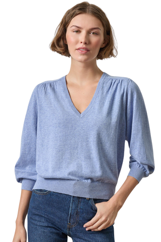 A woman wearing a light blue heathered knit sweater with a V-neck and gathered sleeves, paired with blue jeans, against a plain white background.