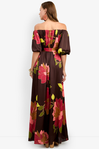 Trina Turk Voglia Dress in Multi featuring a bold floral print, off-the-shoulder neckline, puff sleeves, sash waist, and flowing maxi silhouette.