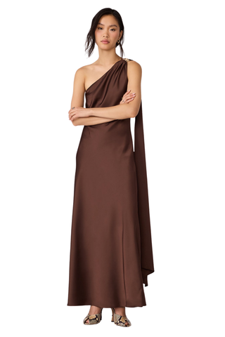 Steve Madden Aurorah Dress in Shaved Chocolate brown featuring a one-shoulder maxi silhouette, gold-tone hardware, and draped back scarf detail.