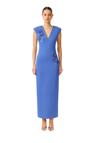 Model wearing the Elliatt Talitha Maxi Dress in Cornflower Blue featuring a plunging V-neckline, structured shoulders, floral appliqué detailing, and a slim column silhouette.