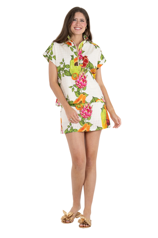 Model wearing the Emily McCarthy Poppy Pullover in Trellis Grove featuring a colorful tropical fruit print, cap sleeves, stand collar, and gold zip neckline