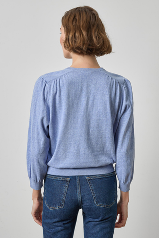 Person wearing a blue sweater and jeans against a plain background