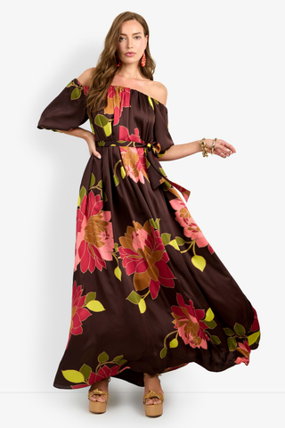 Trina Turk Voglia Dress in Multi featuring a bold floral print, off-the-shoulder neckline, puff sleeves, sash waist, and flowing maxi silhouette.