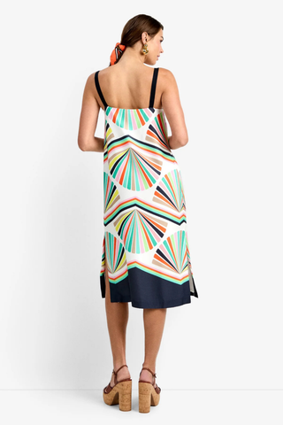Woman wearing a multi-colored geometric print midi dress with thin straps and relaxed fit by Trina Turk, styled with platform sandals on a white background.