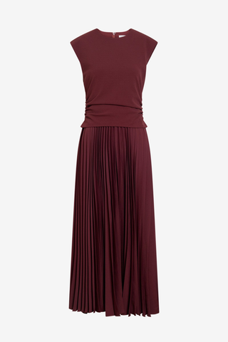 Tanya Taylor Carly Dress in Deep Redwood burgundy with cap sleeves, a ruched fitted waist, and flowing pleated midi skirt.