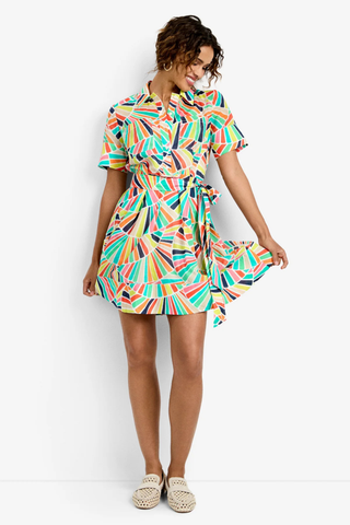 Woman wearing a multi-colored geometric print wrap mini dress with short sleeves and waist tie from Trina Turk on a white background.