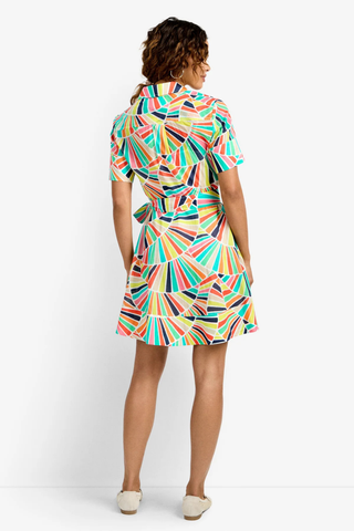 Woman wearing a multi-colored geometric print wrap mini dress with short sleeves and waist tie from Trina Turk on a white background.