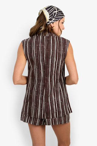 Woman wearing a sleeveless brown dress with white stripes and a headscarf on a white background