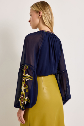 Marie Oliver Royce Blouse in Sundown featuring deep navy fabric, colorful embroidery, a tie neckline, and billowy sleeves.