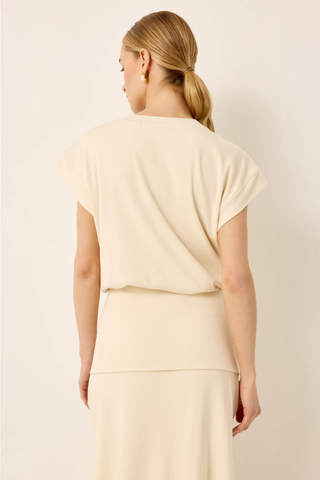Woman wearing a light-colored outfit against a plain background