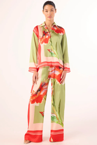 Model wearing the MISA Jaya Top in Scarf Flora Satin featuring a vibrant floral print, satin fabric, button-front closure, long sleeves, and relaxed draped fit paired with coordinating pants