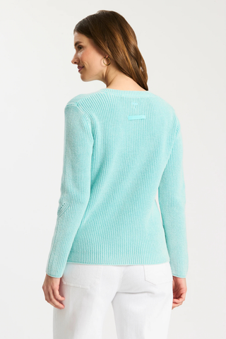 A woman shown from the back wearing a light mint green ribbed knit sweater and white pants against a plain white studio background.
