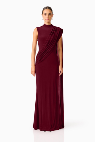 Elliatt Tuloria Sash Gown in Burgundy Red featuring an elegant floor-length silhouette, high neckline, sleeveless design, and dramatic asymmetric draped sash.