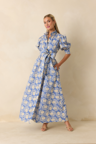 Model wearing the Prosperina Marianne Maxi Dress in Bloomport Print featuring a blue floral print, fitted bodice, and flowing full-length skirt.