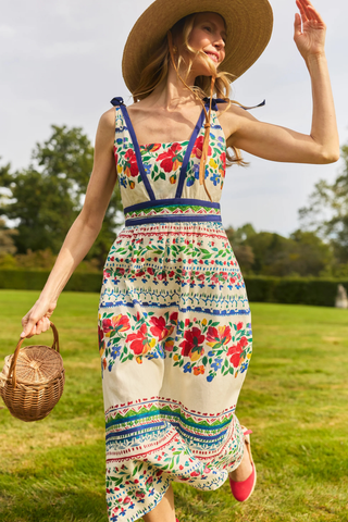 Woman in a colorful dress and straw hat standing in a grassy field.