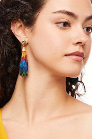 Model wearing the Brackish Leigh Statement Earring featuring handcrafted emerald green, royal blue, red, and yellow natural feathers with a 24K gold-plated stud and elongated teardrop silhouette.
