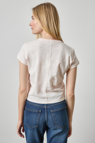 A woman shown from the back wearing a short-sleeve cream-colored t-shirt and blue jeans, photographed against a neutral light gray studio background.