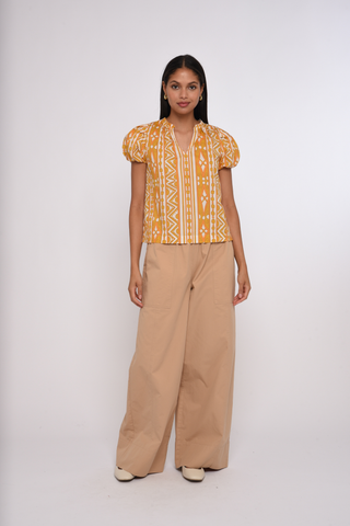 Model wearing the Love the Label Lia Top in Bowen Deco Print featuring puff sleeves and a golden geometric print.