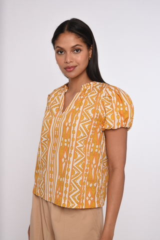 Model wearing the Love the Label Lia Top in Bowen Deco Print featuring puff sleeves and a golden geometric print.