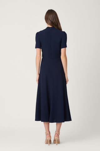 Shoshanna Waldorf Dress in navy featuring a draped V-neckline, short sleeves, gold waist detail, and flared midi skirt.
