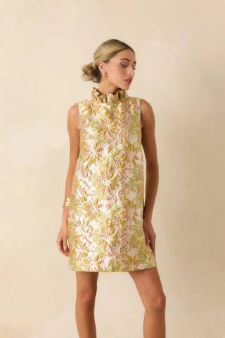 Model wearing Prosperina Cecily Mini Dress in Bombshell Botanicals featuring floral jacquard fabric, ruffle neckline, and oversized bow back detail