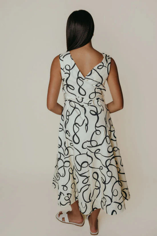 Woman wearing a white dress with black abstract pattern against a plain background