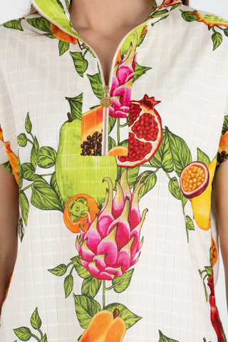 Model wearing the Emily McCarthy Poppy Pullover in Trellis Grove featuring a colorful tropical fruit print, cap sleeves, stand collar, and gold zip neckline