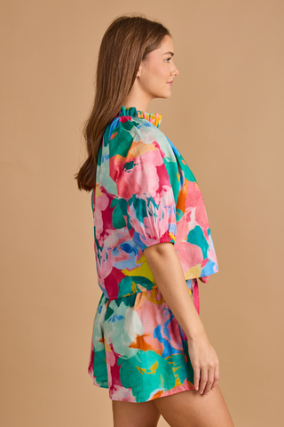 Model wearing the Double A Trish Top in Bougainville featuring a colorful floral print, puff sleeves, gathered ruffle collar, and relaxed silhouette paired with matching shorts